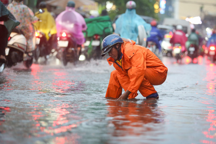 Nhân viên thoát nước mở nắp cống để nước thoát tại đường Ung Văn Khiêm, quận Bình Thạnh - Ảnh: PHƯƠNG QUYÊN